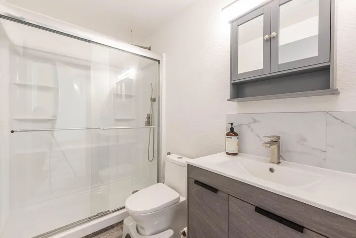 Contemporary bathroom featuring a spacious shower with sliding glass doors, a vanity with wood-finish cabinetry, a white rectangular sink, a single-handle faucet, and a wall-mounted mirrored medicine cabinet