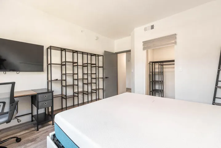 Bright room featuring wood-finish flooring, a built-in closet with shelving, and a wall-mounted shelving unit