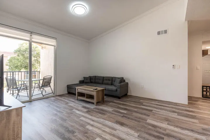 Open living area featuring wood-finish flooring, crown molding, and a flush-mount ceiling light