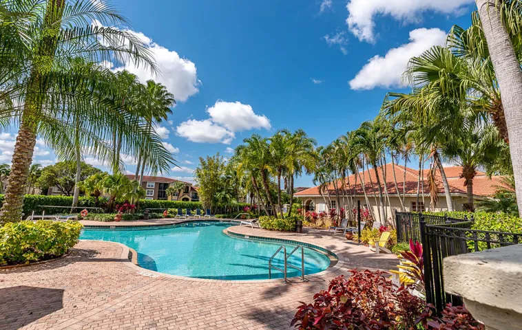 Resort-style pool with brick paver decking, surrounded by mature palm trees and lush landscaping