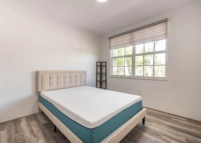 Bright room featuring wood-finish flooring, a large window with horizontal blinds, and textured white walls