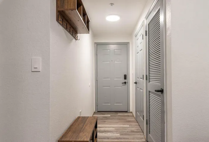 Entryway featuring a light gray door with dark hardware, louvered closet doors, and wood-finish flooring