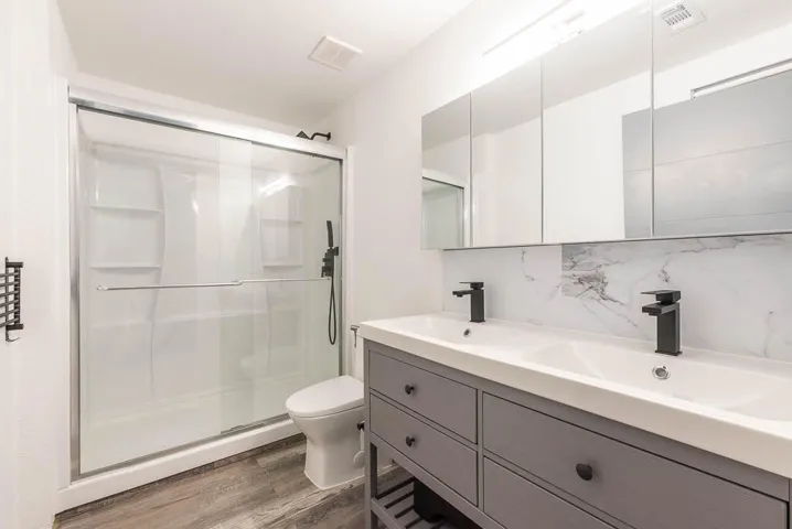 Bathroom featuring a dual-sink vanity with matte black faucets, a mirrored medicine cabinet, and a walk-in shower with a sliding glass door