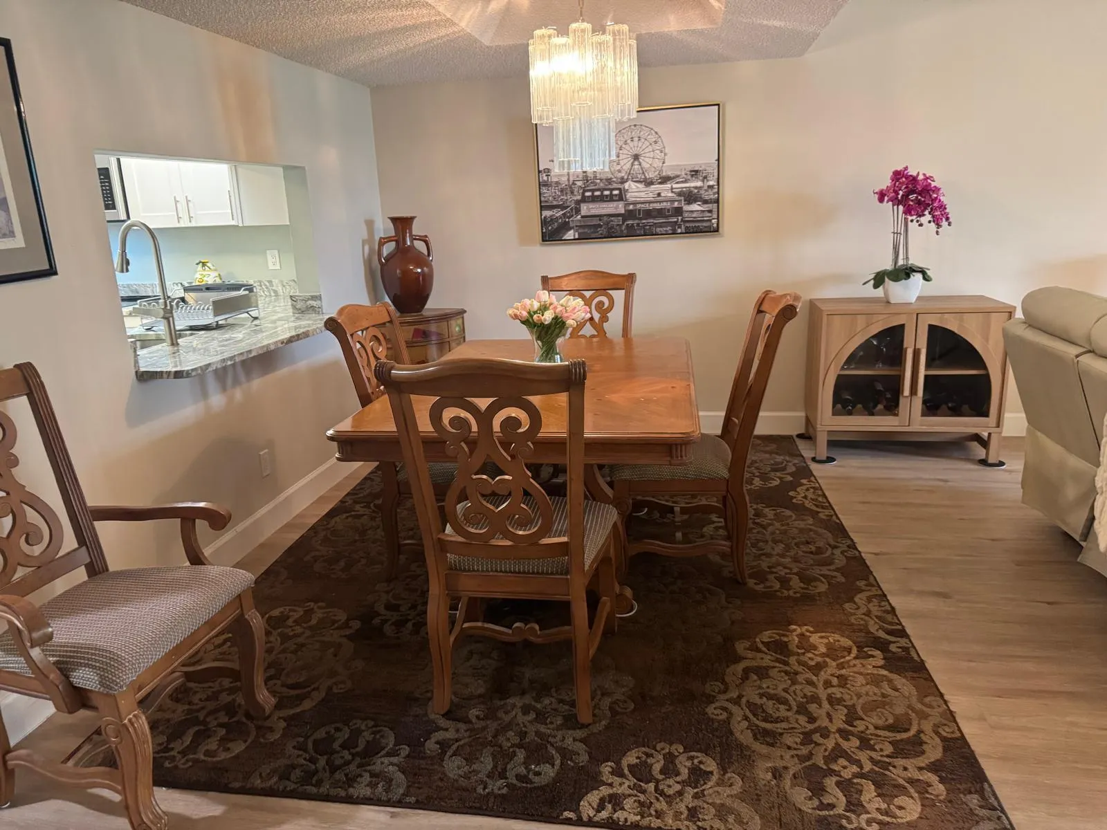 Dining area featuring wood-finish flooring, a contemporary chandelier, and a pass-through window with a granite countertop into the kitchen