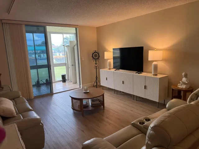 Spacious living area featuring wood-finish flooring, neutral wall tones, and sliding glass doors opening to an enclosed patio