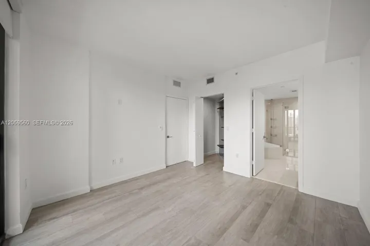 Room featuring wood-finish flooring, crisp neutral walls, a walk-in closet with built-in shelving, and an attached bathroom with a glass-enclosed shower