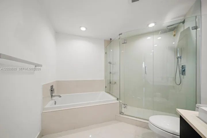 Bathroom featuring a drop-in soaking tub, a frameless glass-enclosed shower, polished tile flooring, recessed lighting, and wall-mounted metal fixtures