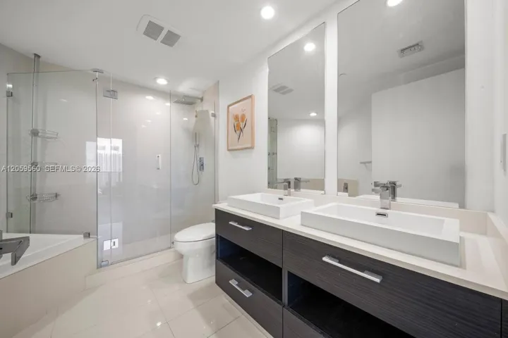 Dual-sink vanity with dark-finish cabinetry, rectangular vessel sinks, frameless glass shower enclosure, and polished tile​​‌​​​​‌​​‌‌​‌‌​​​‌‌​‌​‌​‌​​​‌​​ flooring