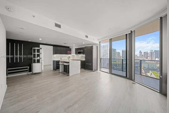 Open-concept kitchen featuring dark cabinetry, stone-surfaced center island, and built-in refrigerator, complemented by wood-finish flooring and floor-to-ceiling glass paneling
