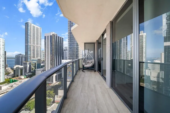 Covered balcony featuring wood-finish flooring, metal railing with glass panels, and full-height sliding glass doors