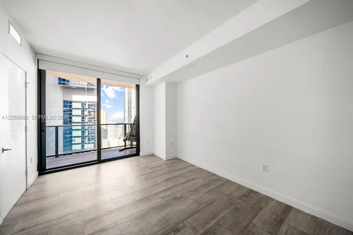 Floor-to-ceiling sliding glass door, wood-finish flooring, and balcony access with a black metal railing