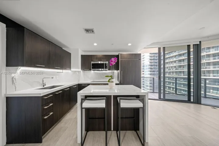 Kitchen featuring dark wood-finish cabinetry, solid-surface countertops, a waterfall-edge kitchen island, integrated appliances, and sliding glass balcony doors