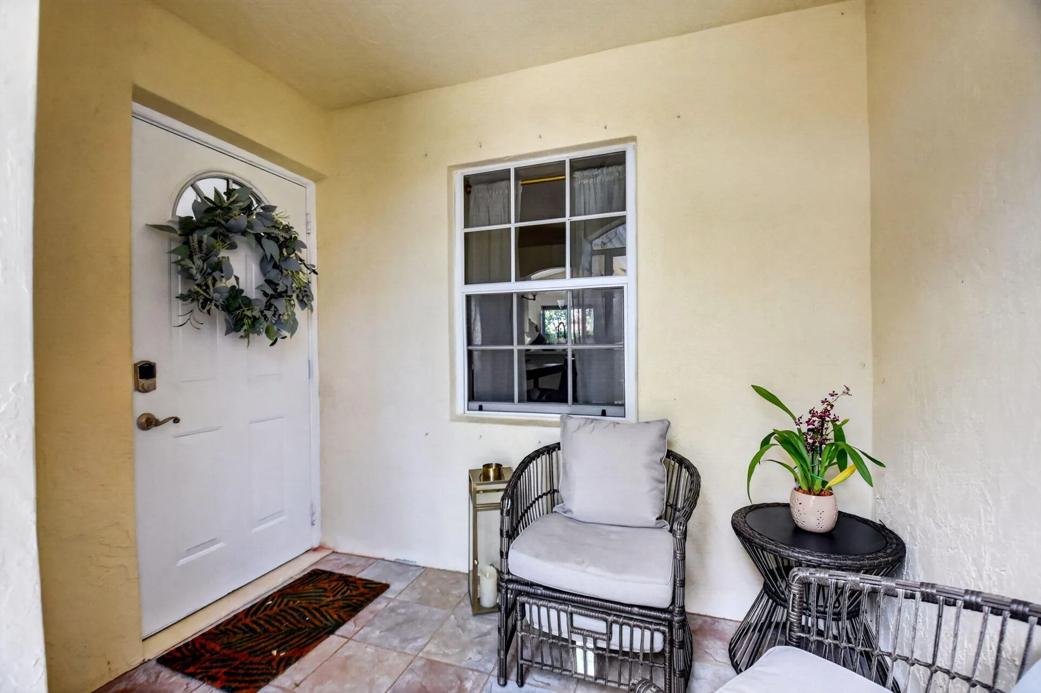 Covered porch entry featuring a white door with an arched glass insert, a grid-paned window, textured yellow exterior walls, and tiled flooring