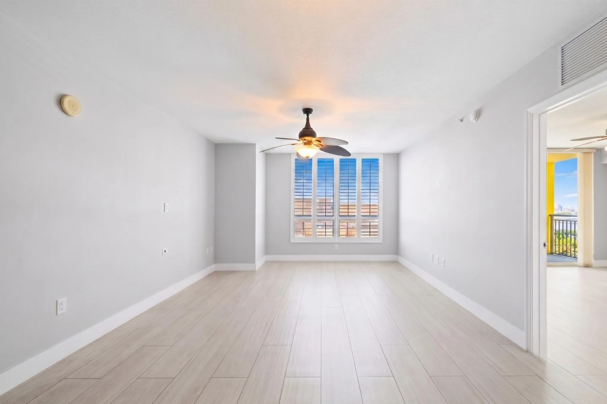 Spacious living & dining areas with light wood-look porcelain tile flooring, a ceiling fan & large windows framing downtown Fort Lauderdale views.