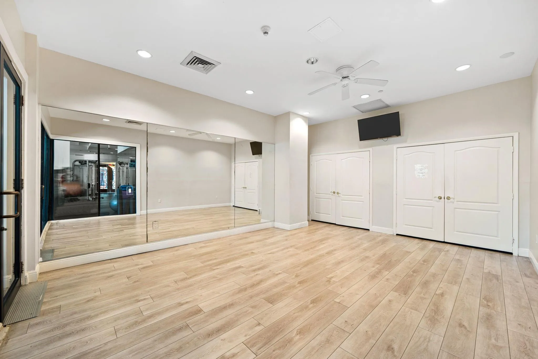 Dedicated studio for yoga, stretching & private fitness routines, featuring mirrored walls & wood flooring.