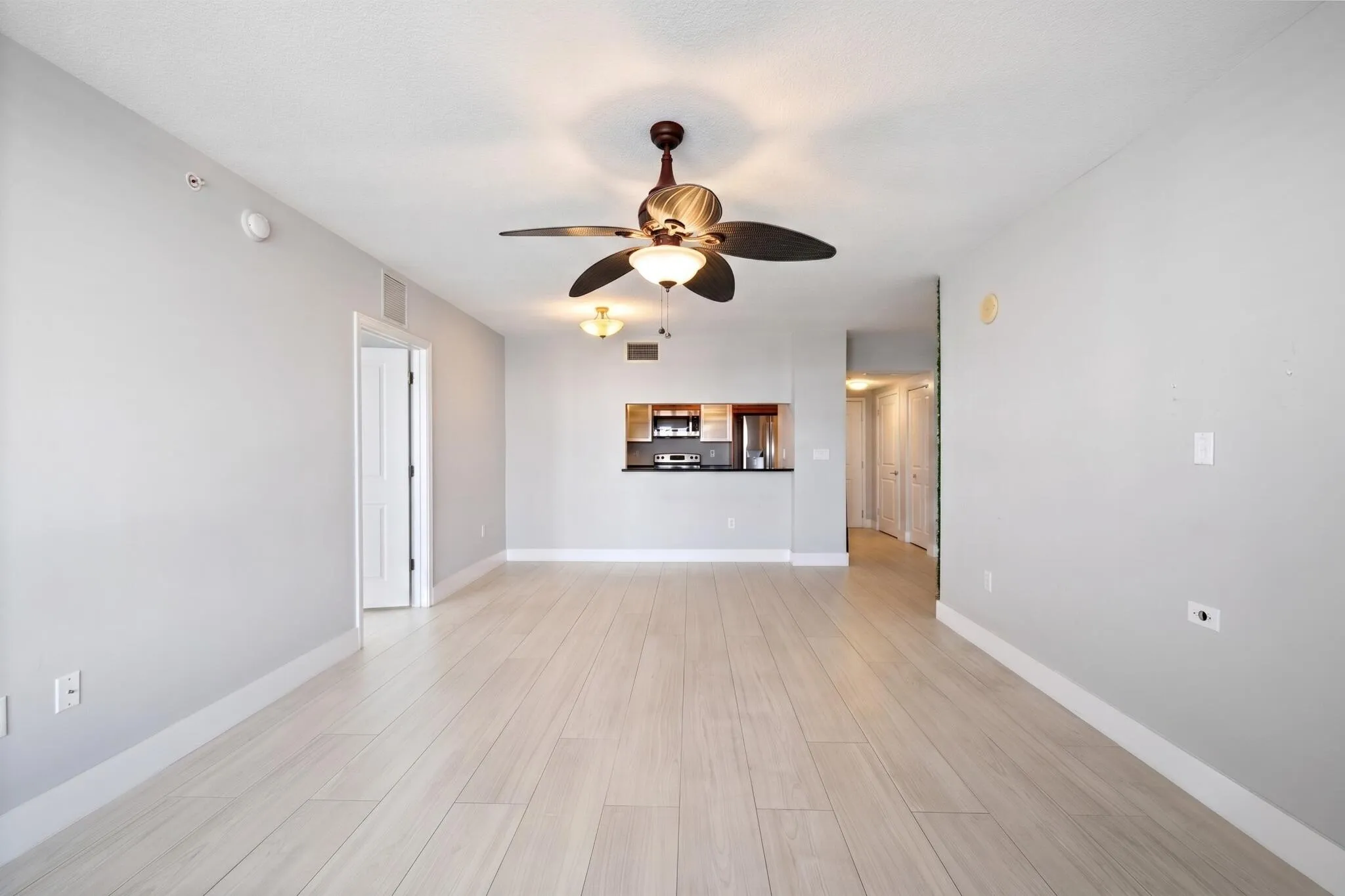 Wide view of the open living & dining areas, featuring a kitchen pass-through, ceiling fans & a natural connection between the main gathering spaces.