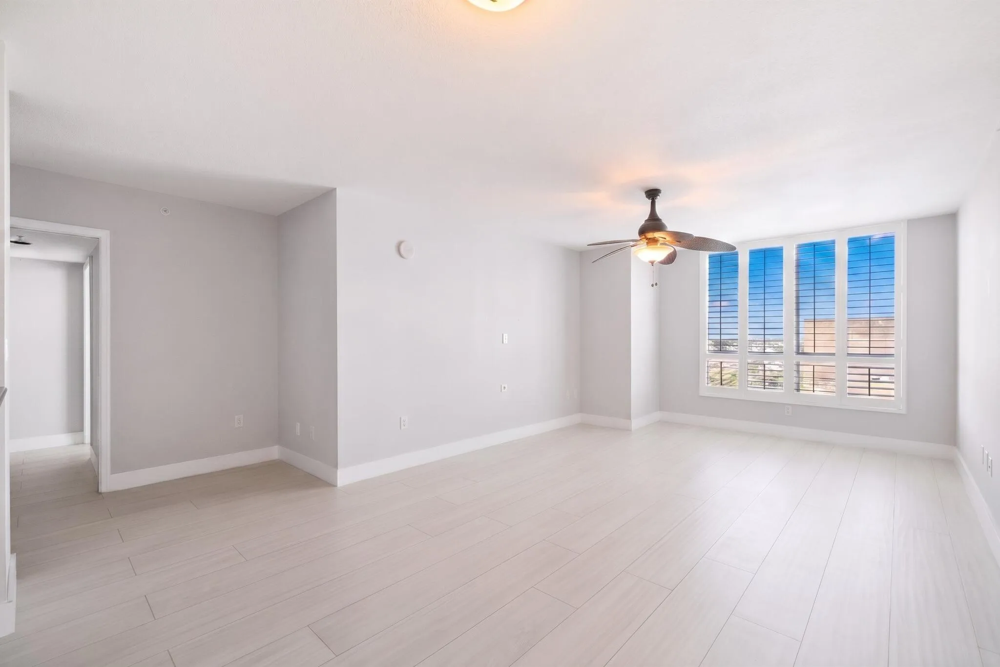 Bright, open living area with light wood-look porcelain tile flooring, large windows with plantation shutters & flexible space for relaxing or entertaining.