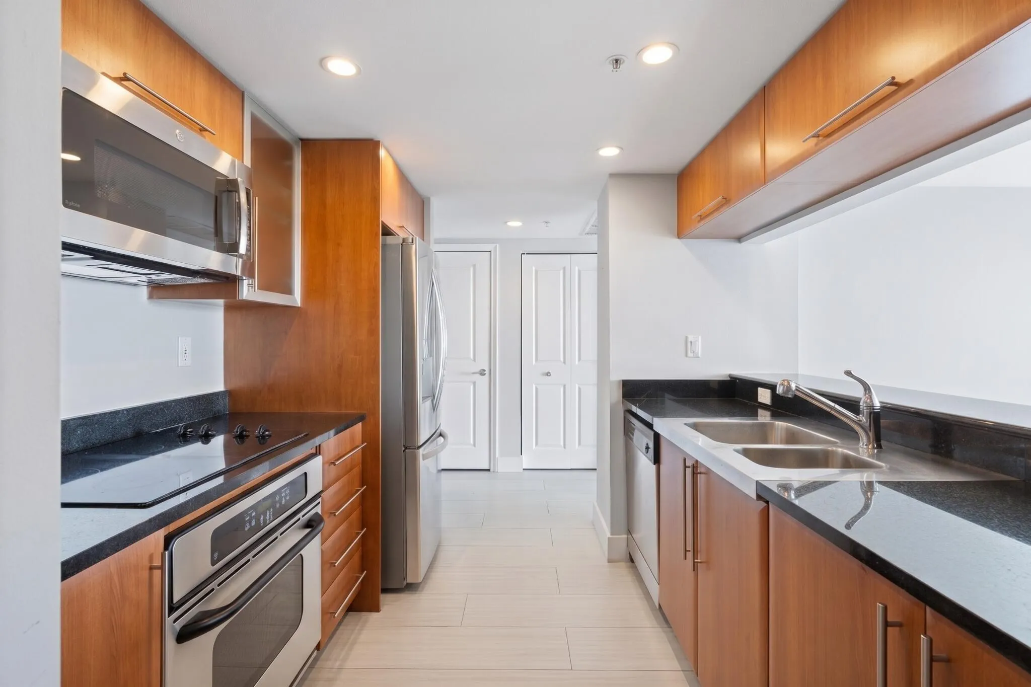 Alternate kitchen view highlighting stainless-steel appliances, a double-basin sink, pantry storage, granite countertops & tile flooring.