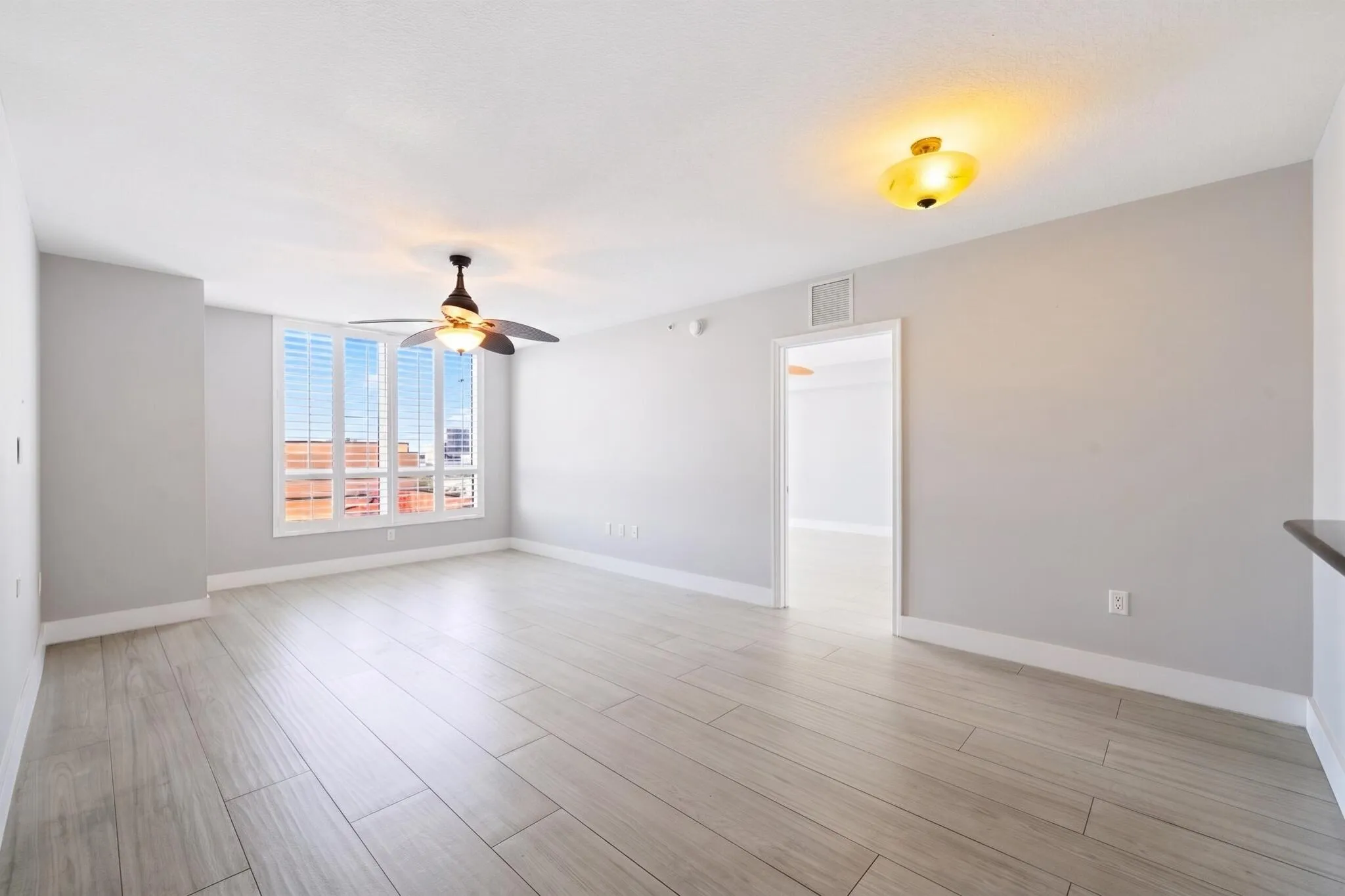 Alternate living room view highlighting the generous proportions, porcelain tile flooring & large window with plantation shutters.