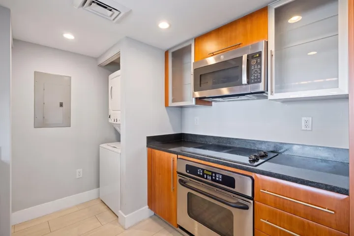 Kitchen cooking area with a glass electric cooktop, built-in oven & microwave, granite countertops & select frosted-glass upper cabinets.