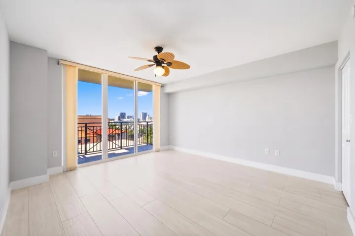 Generously sized main suite with light wood-look porcelain tile flooring, a ceiling fan & sliding glass doors opening to a private covered terrace with New River & downtown Fort Lauderdale views.