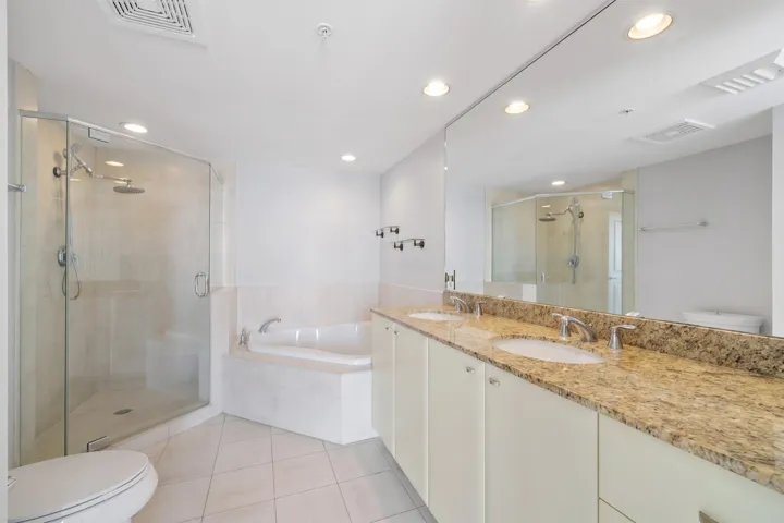 Spa-like main bathroom featuring a long dual-sink granite vanity, oversized soaking tub & separate glass-enclosed walk-in shower.