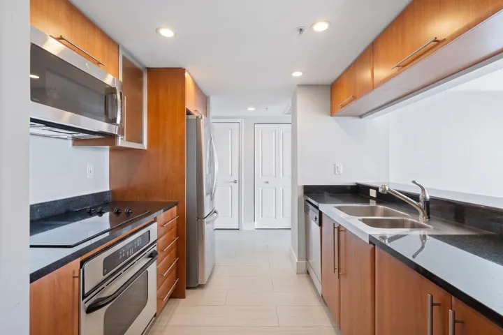 Alternate kitchen view highlighting stainless-steel appliances, a double-basin sink, pantry storage, granite countertops & tile flooring.