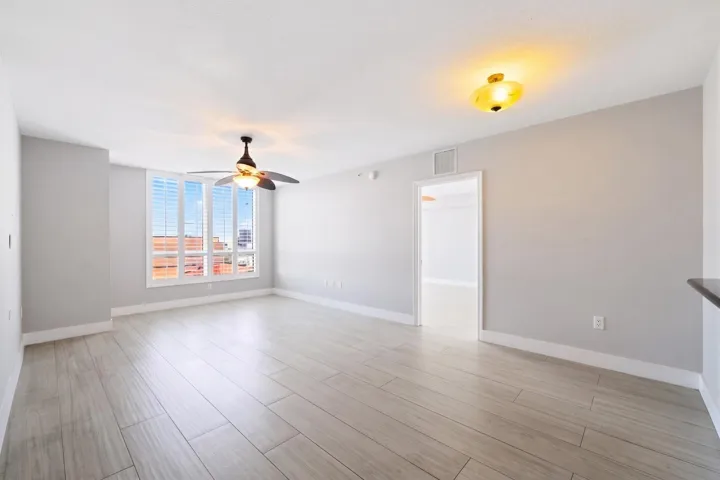 Alternate living room view highlighting the generous proportions, porcelain tile flooring & large window with plantation shutters.