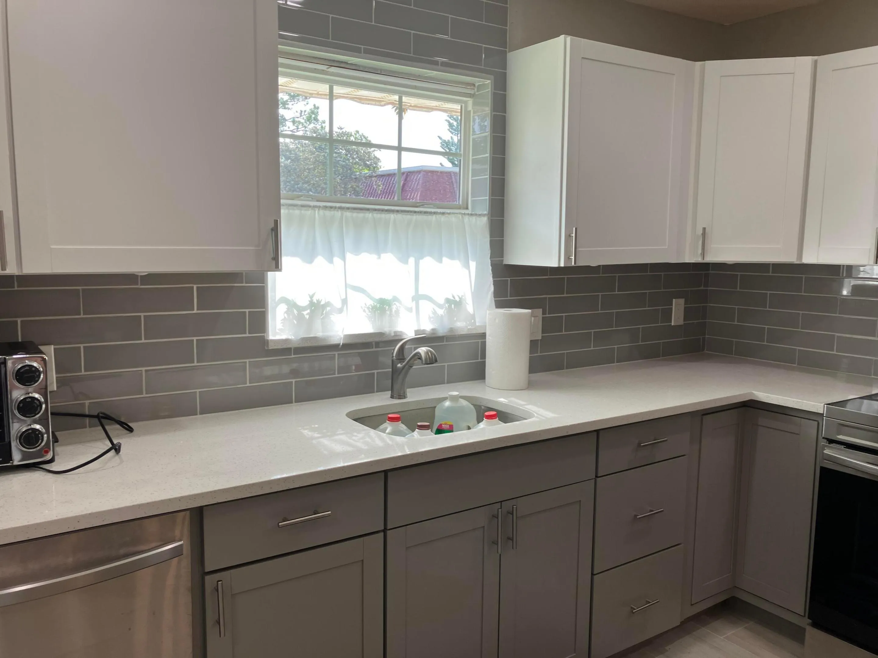 Contemporary kitchen featuring gray subway tile backsplash, light-toned countertops, and a stainless steel undermount sink