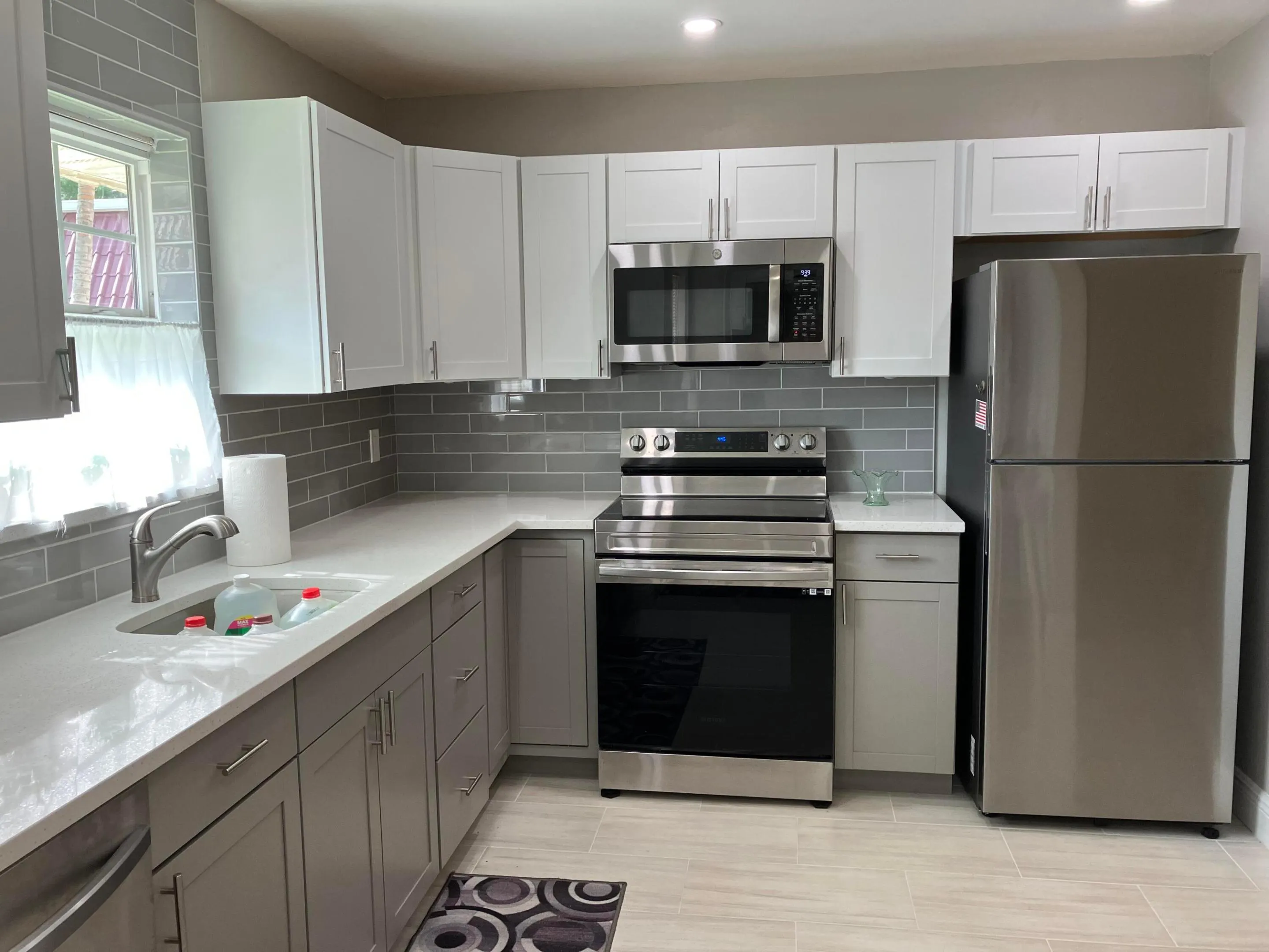 Contemporary kitchen featuring two-tone cabinetry, stainless steel appliances, a subway tile backsplash, light-colored countertops, and wood-finish tile flooring