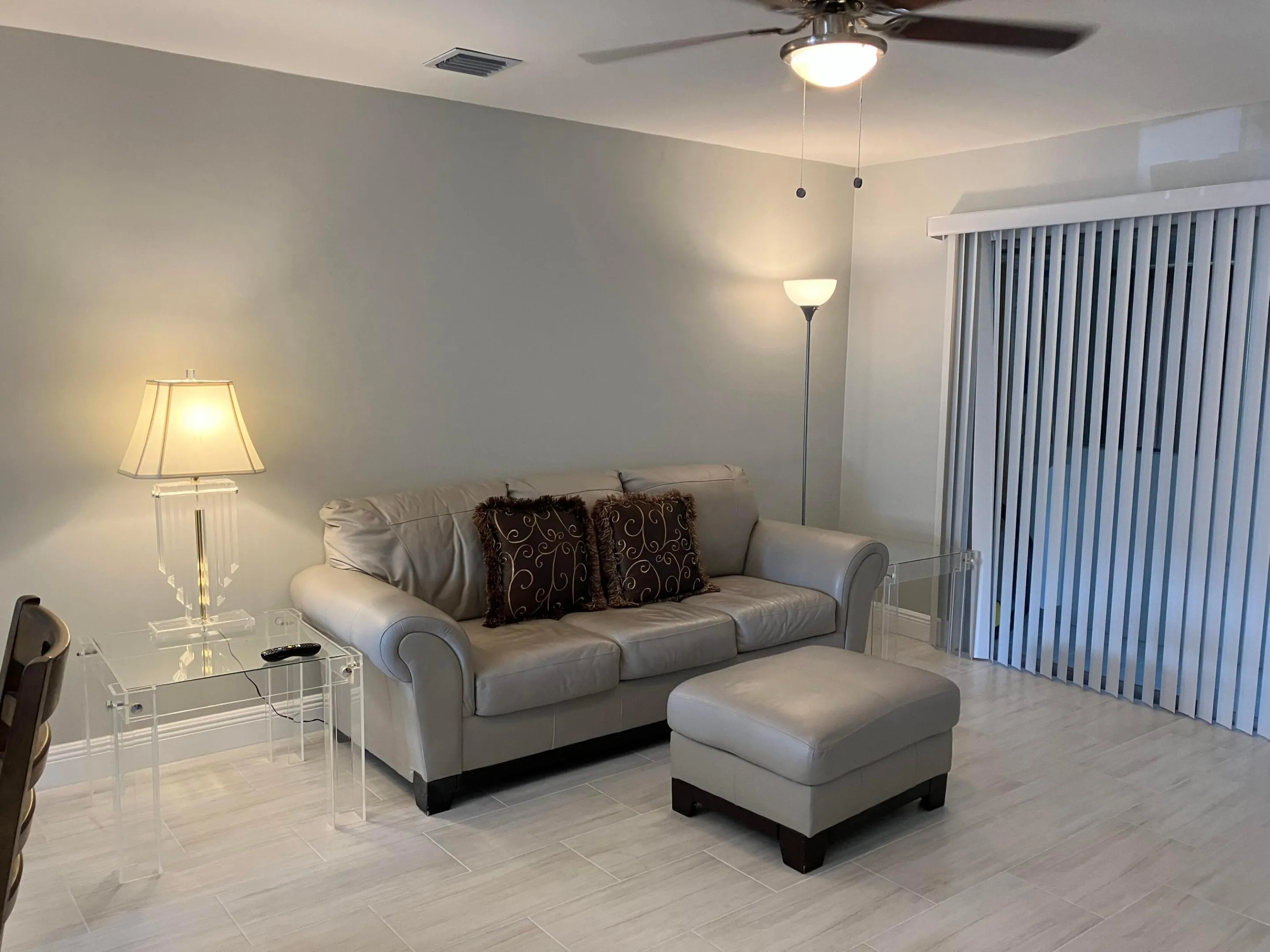 Spacious living area featuring light-toned walls, wood-finish flooring, and a ceiling fan with integrated lighting