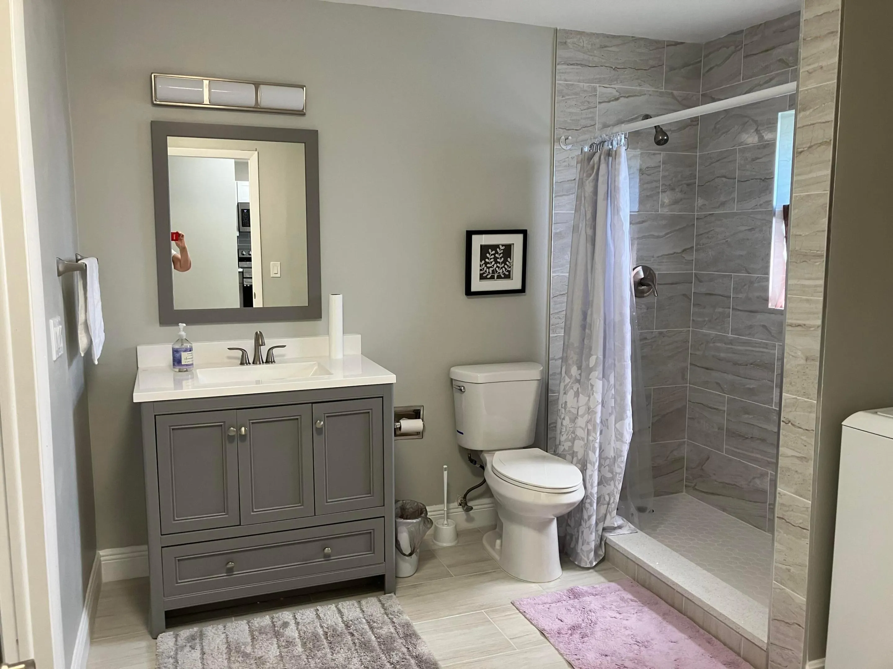 Full bathroom featuring a grey vanity with a white countertop and integrated sink, brushed nickel faucet, and a wall-mounted mirror