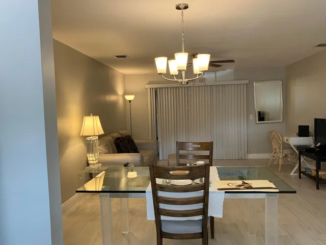Dining area featuring wood-finish flooring, a contemporary chandelier, and a glass-top dining table