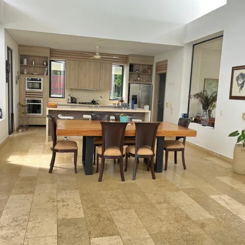 Open-concept kitchen and dining area featuring light-toned tile flooring, light wood-finish cabinetry, built-in double ovens, and a stainless steel refrigerator