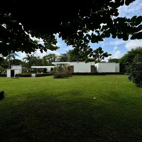 Expansive green lawn with a contemporary white residence featuring multiple structures, a covered outdoor area, and a swimming pool