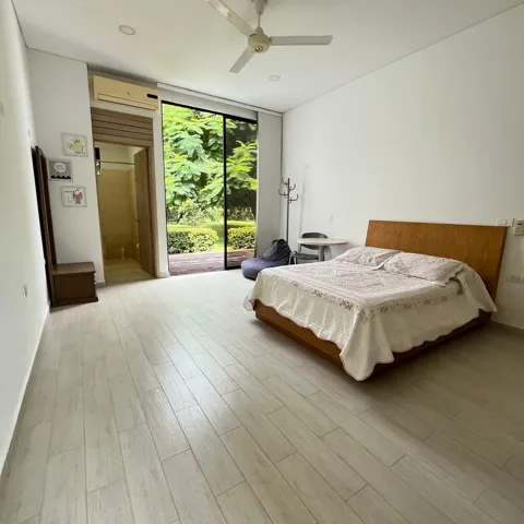 Spacious room featuring light wood-finish flooring, a ceiling fan, and a large sliding glass door offering direct access to outdoor greenery