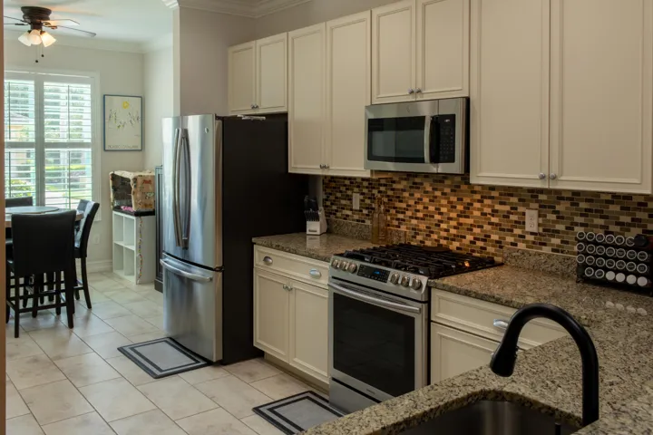 Kitchen featuring granite countertops, stainless steel appliances, mosaic tile backsplash, cream cabinetry, and tile flooring