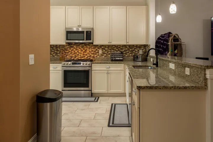 Kitchen with cream cabinetry, stainless steel appliances, a mosaic tile backsplash, and granite countertops
