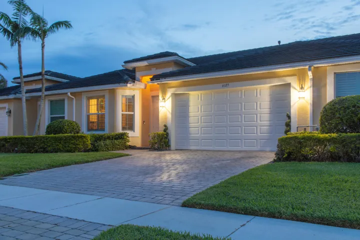 Single-story residence featuring a tile roof, stucco exterior, patterned garage door, paver driveway, and manicured landscaping