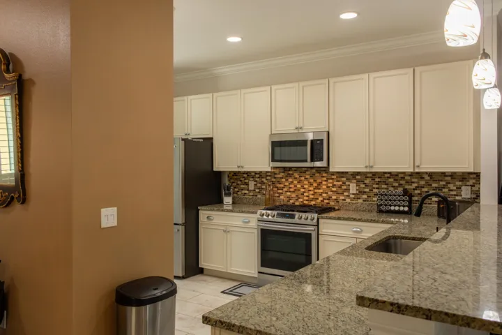 Kitchen featuring light-toned cabinetry, stainless steel appliances, speckled stone countertops, a mosaic tile backsplash, and recessed lighting