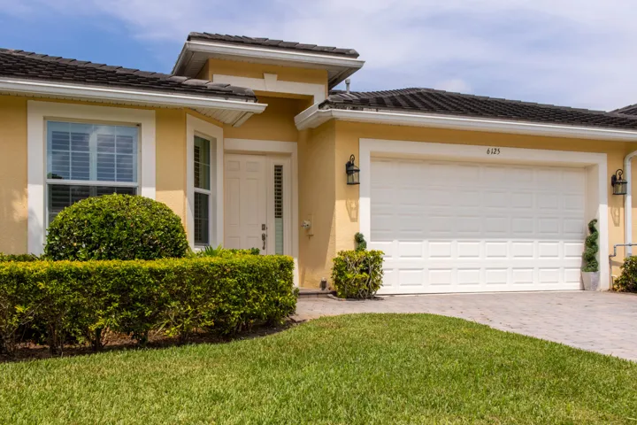 Contemporary stucco exterior featuring a two-car garage with panel detailing, decorative exterior lighting, and a paved driveway