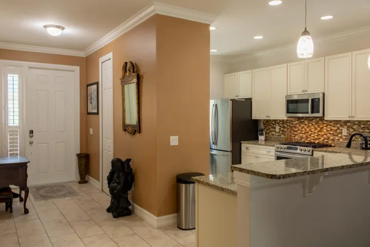 Open-concept kitchen with granite countertops, white cabinetry, stainless steel appliances, and a mosaic tile backsplash