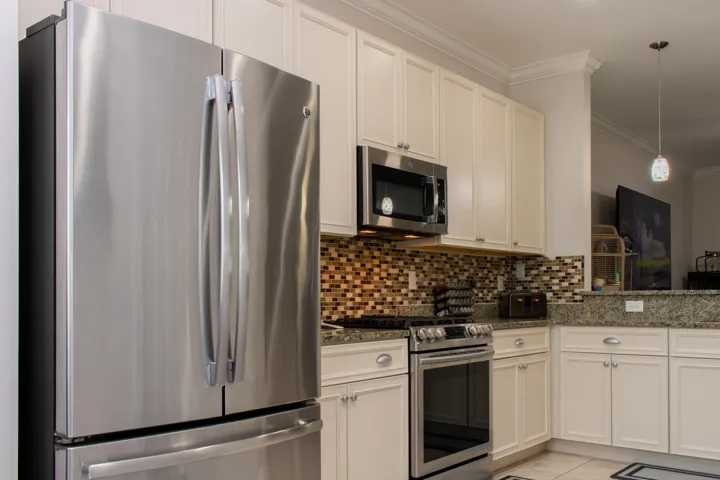 Kitchen featuring stainless steel appliances, light cabinetry with crown molding, granite countertops, and a mosaic tile backsplash