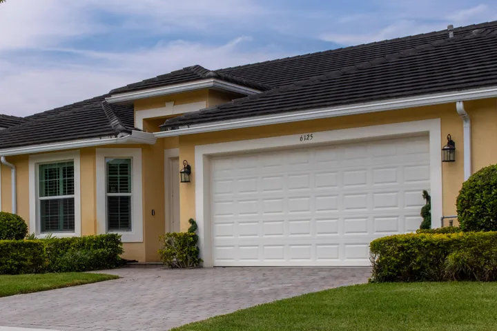 Single-story residence featuring a two-car garage with panel detailing, a dark tile roof, and a paver driveway