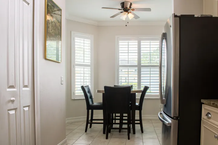 Dining area featuring two large windows with white louvered shutters, a ceiling fan with integrated lighting, and neutral-toned tile flooring