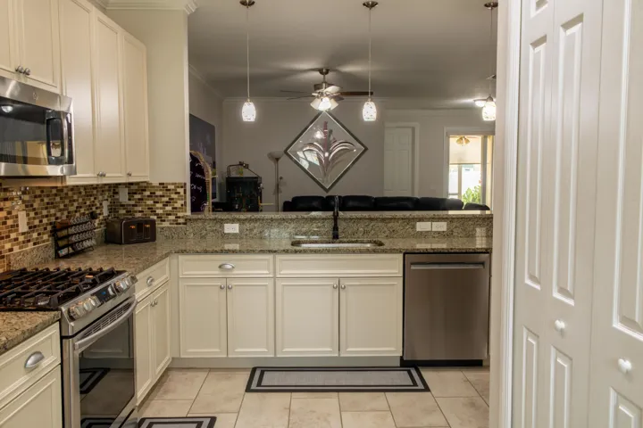 Kitchen featuring cream cabinetry, granite countertops, stainless steel appliances, a tile backsplash, and tile flooring