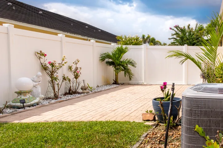 Private outdoor space featuring a paver patio, lush green lawn, mature landscaping, and white vinyl fencing