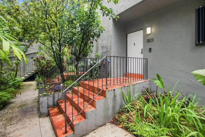 Exterior entry featuring red brick stairs, black metal railings, a white entry door, and a modern exterior light fixture