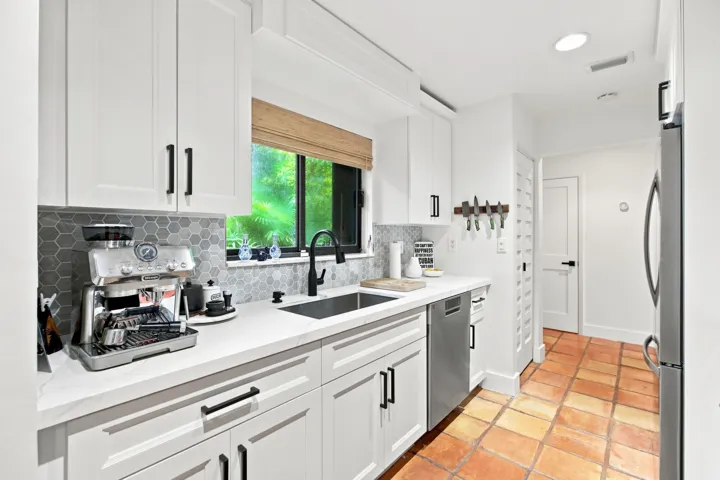 Modern kitchen featuring white shaker cabinetry, stainless steel dishwasher, hexagonal tile backsplash, and a large window above the sink