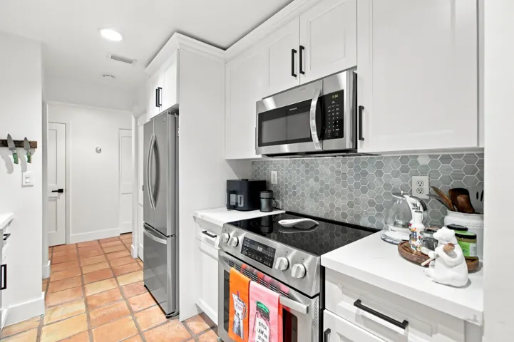 Kitchen featuring white cabinetry, stainless steel appliances, a hexagonal tile backsplash, white countertops, and terracotta-style floor tiling